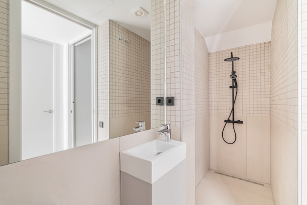 Interior del cuarto de baño moderno con ducha de azulejos beige y lavabo pequeño