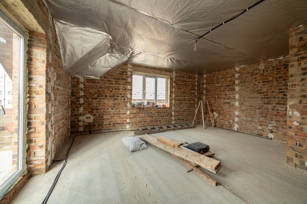 Interior da casa de tijolo inacabado com piso de concreto e paredes nuas prontas para reboco em construção. Incorporação imobiliária