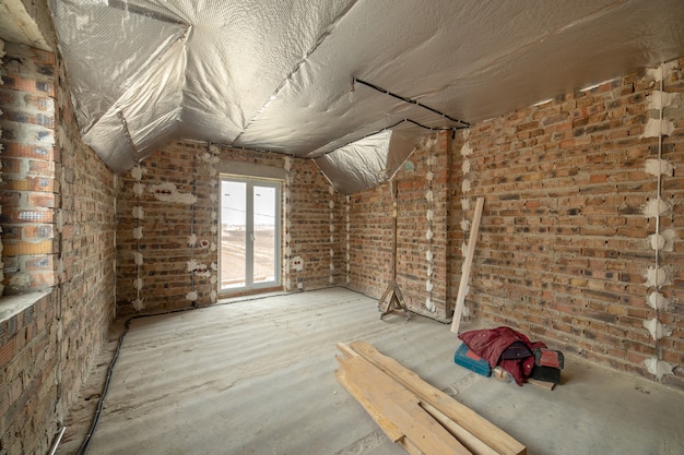 Interior da casa de tijolo inacabado com piso de concreto e paredes nuas prontas para reboco em construção. Incorporação imobiliária