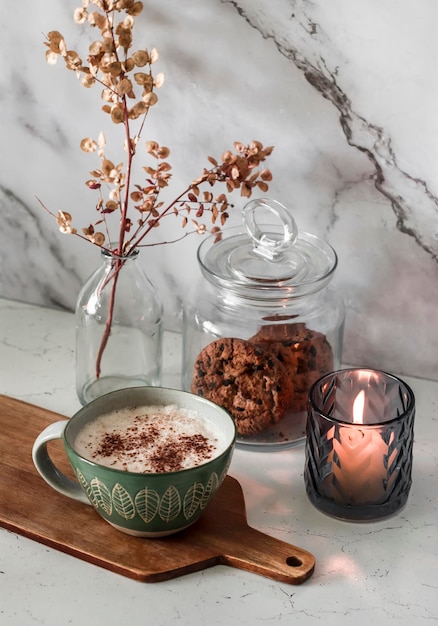 Interior da cozinha aconchegante da manhã Cappuccino acendeu biscoitos de vela em uma jarra de flores secas em um vaso sobre a mesa