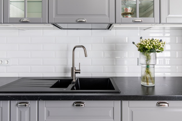 Interior Da Cozinha Moderna. Bancada e pia escuras, frentes de armário cinza. Vaso com flores decora a mesa