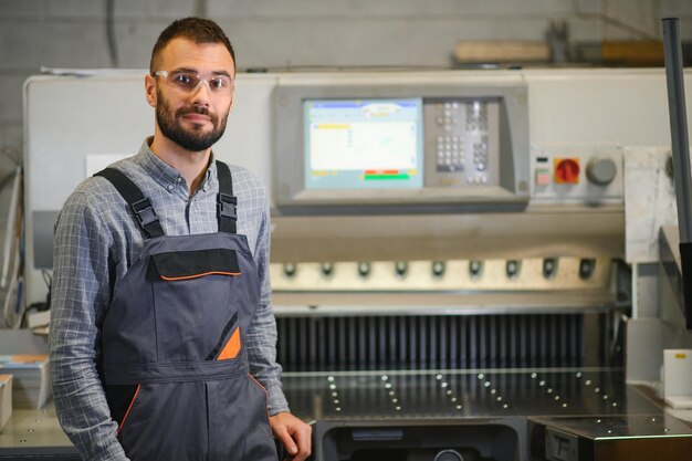 Interior da impressora com moderna máquina de impressão offset e operador em uniforme de trabalho verificando a qualidade e controlando o processo de impressão