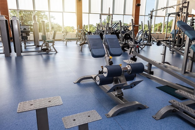 Interior da moderna sala de ginástica com equipamentos esportivos e de condicionamento físico contra as grandes janelas