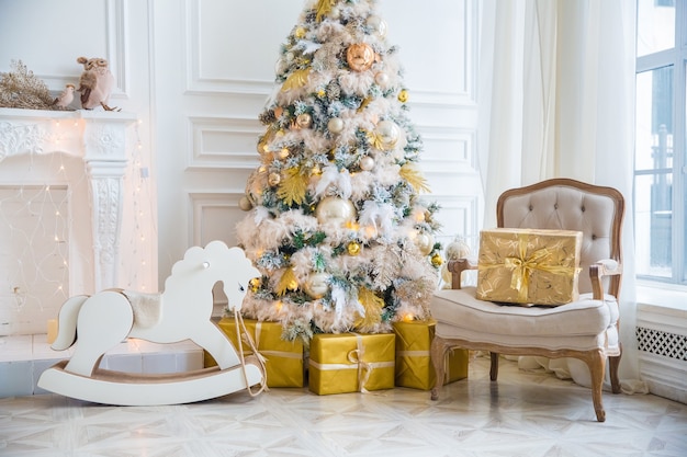 Interior da sala branca com árvore de Ano Novo decorada, caixas de presentes e lareira artificial