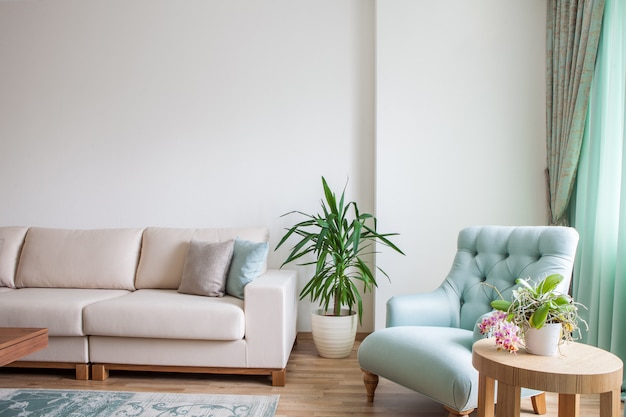 Interior da sala de estar com sofá branco, poltrona de hortelã e uma mesa de café de madeira decorada com plantas.