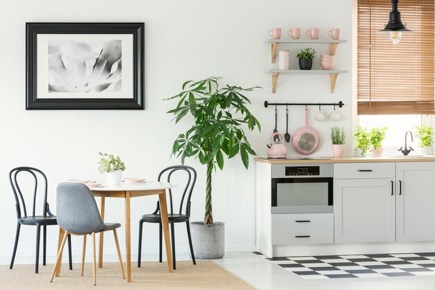 Interior da sala de jantar de espaço aberto com uma pintura de cadeiras de mesa e árvore ao lado de um interior de cozinha com ferramentas rosa e piso xadrez