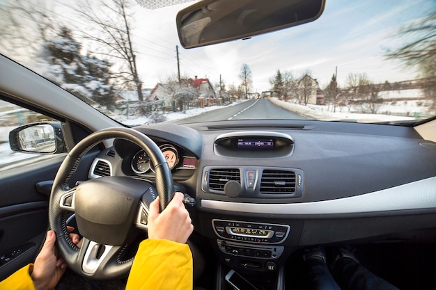 Interior de carro moderno com mãos femininas motorista no volante, paisagem de inverno nevado lá fora. Conceito de condução segura.