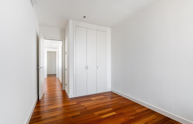 Interior de um apartamento vazio, quarto branco com armário embutido, chão de parquet e vista para o corredor