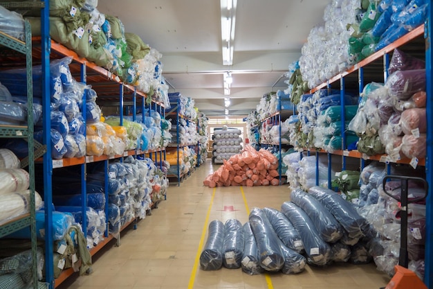 Interior de um armazém industrial com muitas prateleiras com rolos de tecido colorido neles O trabalhador levanta o tecido do rolo e verifica a quantidade