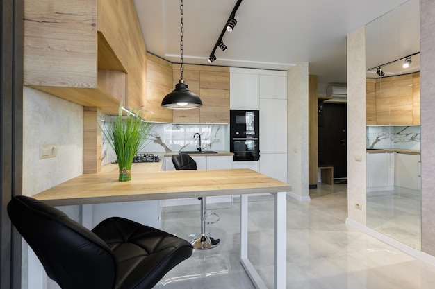 Interior de uma cozinha moderna, com um bar com pastilhas de madeira e azulejos de mármore branco, em um pequeno apartamento