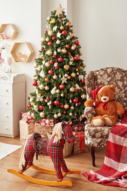 Interior do Natal do quarto infantilNatal no berçário. Cavalo de balanço e urso de brinquedo macio no fundo da árvore de Natal.