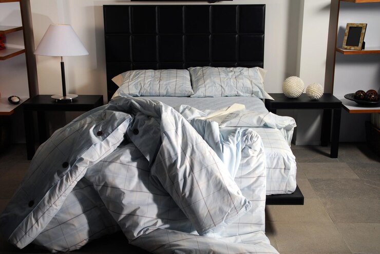 Foto interior do quarto com cama desfeita, mesa de cabeceira, lâmpada e várias decorações modernas, estilo de vida