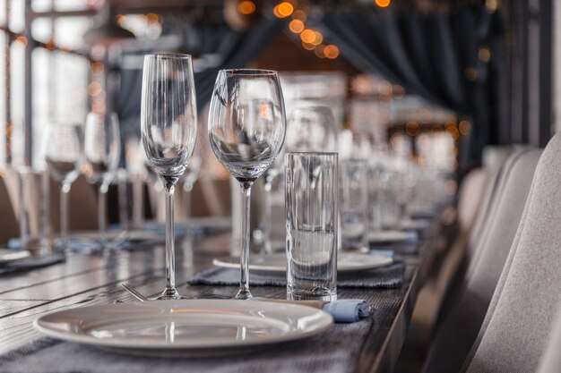 Interior do restaurante, servindo vinho e copos de água, pratos, garfos e facas em guardanapos têxteis fica em uma linha na mesa de madeira cinza vintage