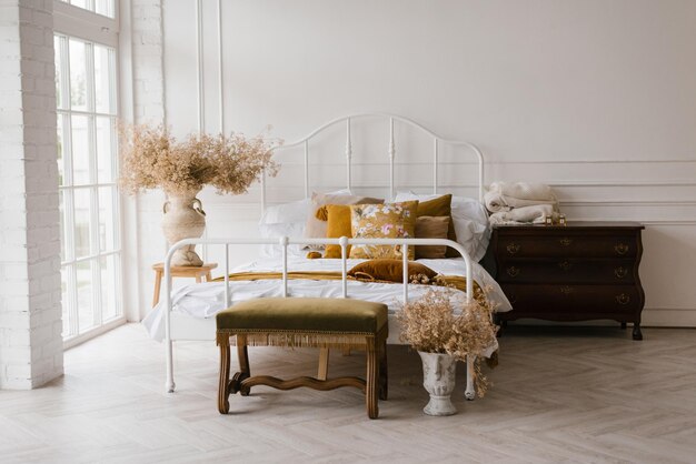 Interior de un dormitorio blanco moderno con una cama doble con almohadas y decoración otoñal flores secas en un jarrón