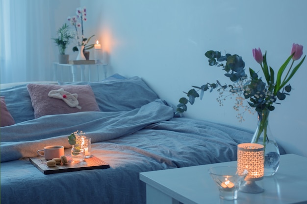 Interior de dormitorio con flores, velas y una taza de té.