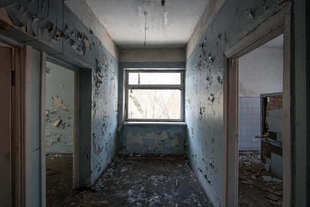 Interior de un edificio de hormigón abandonado con una ventana en el centro y pintura desconchada en las paredes