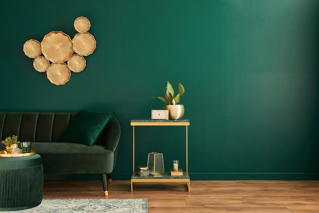 Interior elegante da sala de estar com design moderno, sofá de veludo verde, móveis, decoração dourada, planta, carpete, espaço para cópia, travesseiro e acessórios pessoais elegantes. Modelo.