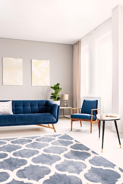 Foto interior elegante da sala de estar com um sofá azul escuro e uma poltrona combinando grandes janelas com cortinas e um tapete decorativo foto real