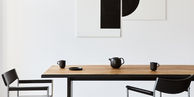 Interior elegante da sala de jantar com mesa de família de madeira de design, cadeiras pretas, bule com caneca, simular pinturas de arte na parede e acessórios elegantes na decoração moderna. Modelo.