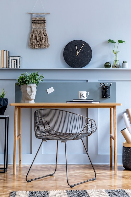 Interior elegante de sala de estar escandinava com mesa de madeira, cadeira, vidraças de madeira com prateleira, abajur, plantas, relógio preto, material de escritório e acessórios elegantes em decoração moderna.