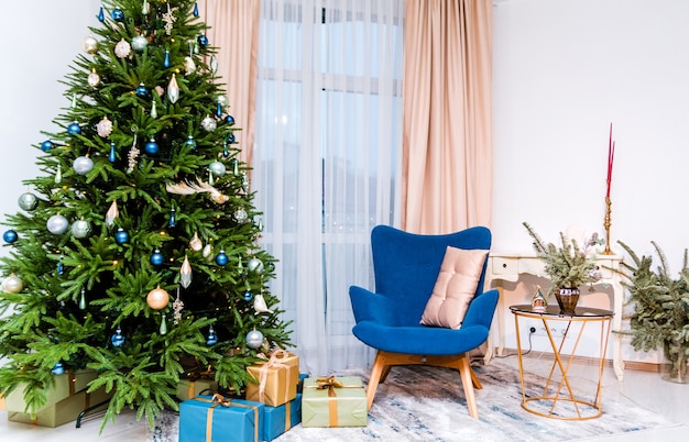 Interior elegante e moderno de ano novo do quarto. No kmnat há uma árvore de natal com presentes, uma poltrona azul, uma mesa com decoração de ano novo. foto