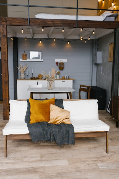 Interior elegante y escandinavo de la sala de estar de un apartamento moderno con un sofá blanco, almohadas, una manta, una cocina en el fondo. Decoración moderna para el hogar.