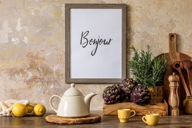 Interior elegante del espacio de la cocina con mesa de madera, marco de fotos marrón, hierbas, verduras, tetera, taza y accesorios de cocina en el concepto wabi sabi de la decoración del hogar.