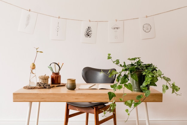 Interior elegante del espacio de la oficina en casa con escritorio de madera, accesorios de bosque, planta de aguacate, estante de bambú, plantas y decoración de ratán