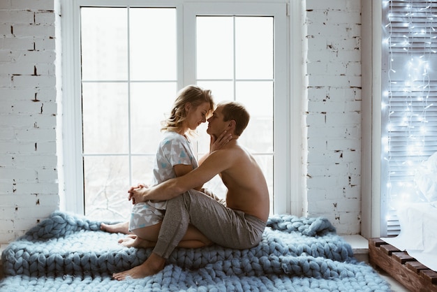 Interior elegante. Um casal perto da janela, debaixo de um cobertor azul de grande acasalamento. História de amor.