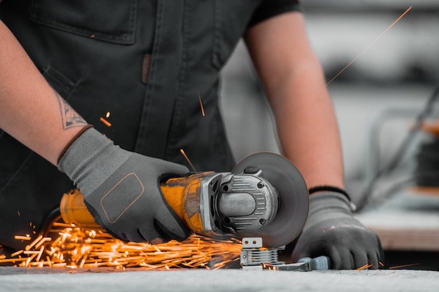 Interior de fábrica de ingeniería de industria pesada con trabajador industrial usando amoladora angular y cortando un tubo de metal. Contratista en Fabricación de Estructuras Metálicas de Uniformes de Seguridad y Cascos. Alta calidad