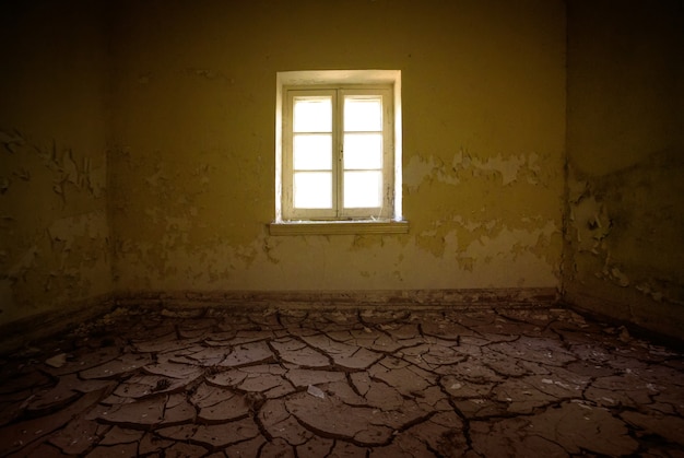 Interior de la habitación en casa abandonada con tierra seca agrietada en el suelo y pintura vieja pelada en las paredes