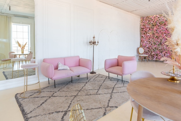 Interior ligero delicado y acogedor de la sala de estar con muebles elegantes y modernos de color rosa pastel y paredes blancas con molduras de estuco a la luz del día