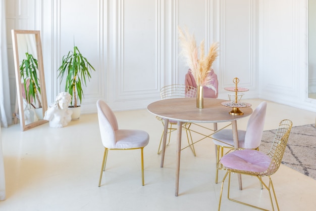 Interior ligero delicado y acogedor de la sala de estar con muebles elegantes y modernos de color rosa pastel y paredes blancas con molduras de estuco a la luz del día