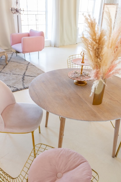 Foto interior ligero delicado y acogedor de la sala de estar con muebles elegantes y modernos de color rosa pastel y paredes blancas con molduras de estuco a la luz del día