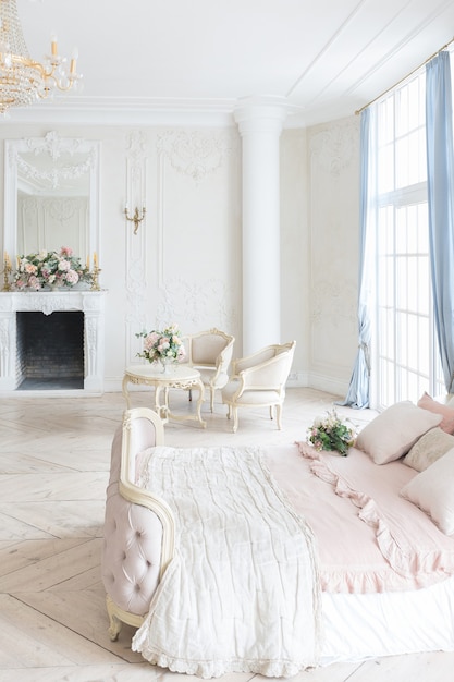 Interior luminoso de lujo en estilo barroco. Una habitación espaciosa con un hermoso mobiliario de carretera elegante, una chimenea y flores. Planta de estuco en las paredes y parquet de madera clara.