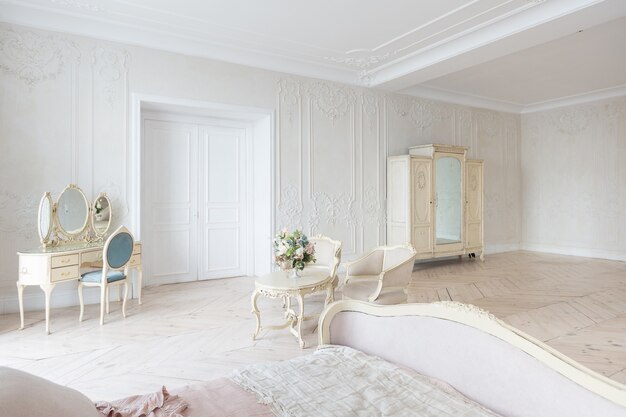 Interior luminoso de lujo en estilo barroco. Una habitación espaciosa con un hermoso mobiliario de carretera elegante, una chimenea y flores. Planta de estuco en las paredes y parquet de madera clara.