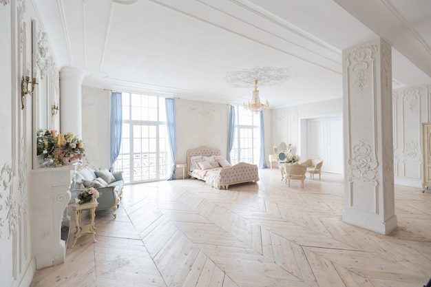 Interior luminoso de lujo en estilo barroco. Una habitación espaciosa con un hermoso mobiliario de carretera elegante, una chimenea y flores. Planta de estuco en las paredes y parquet de madera clara.