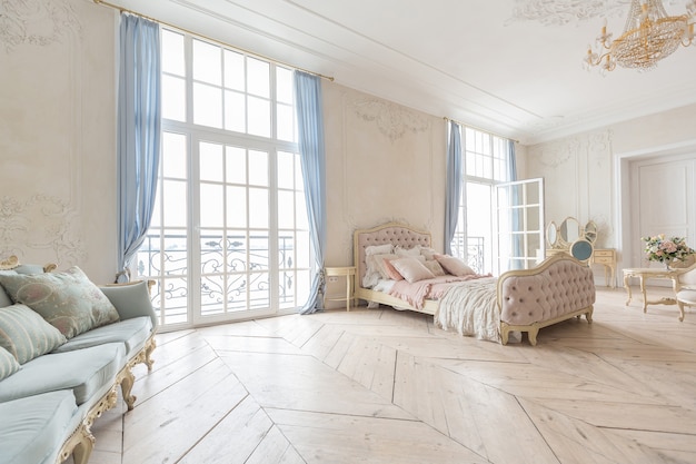 Interior luminoso de lujo en estilo barroco. Una habitación espaciosa con un hermoso mobiliario de carretera elegante, una chimenea y flores. Planta de estuco en las paredes y parquet de madera clara.