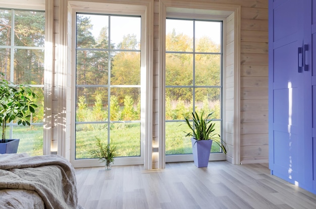 Interior luminoso, quarto em casa de madeira com grande janela com vista para o pátio de outono. Paisagem de outono dourada na janela branca. Cor ano 2022