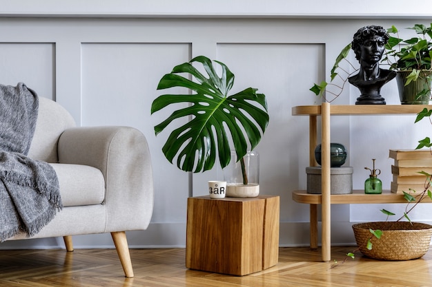 Interior minimalista de la sala de estar con consola de madera, sofá, hermosas plantas, hojas tropicales, libro, cubo, estante, decoración, pared gris y accesorios personales en una elegante decoración para el hogar.