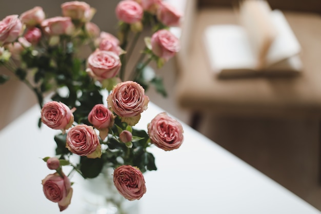 Interior moderno da sala com livro de poltrona e rosas frescas na mesa