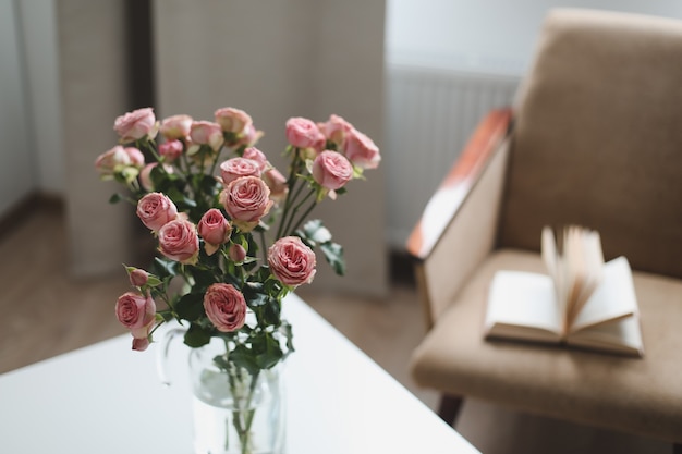 Interior moderno da sala com livro de poltrona e rosas frescas na mesa