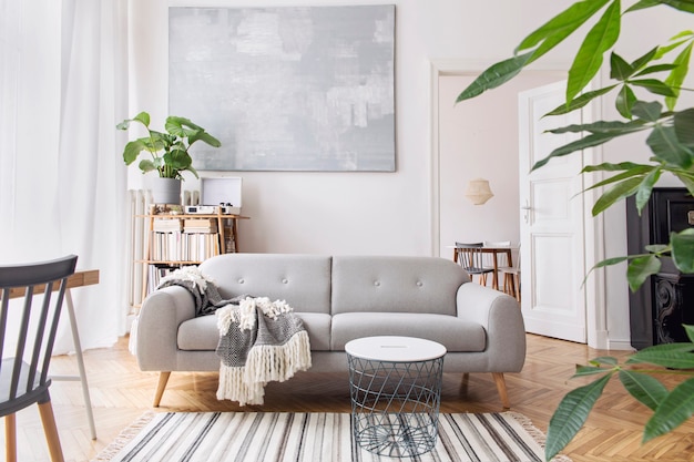 Interior moderno da sala de estar escandinava com sofá de design, cobertor elegante, mesa de centro, estante de livros, plantas e parquet de madeira marrom