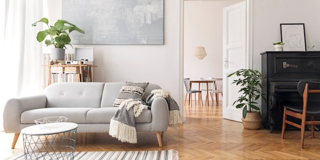 Interior moderno da sala de estar escandinava com sofá de design, cobertor elegante, mesa de centro, estante de livros, plantas e parquet de madeira marrom