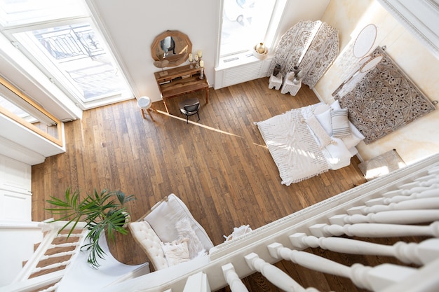 Interior moderno de um quarto bem iluminado em um apartamento de dois andares com itens decorativos em estilo bali com varanda. paredes brancas, pisos de madeira e móveis vintage