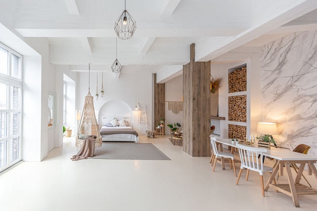 Interior moderno de moda de un apartamento estudio ligero con columnas de madera en estilo loft, decorado con ladrillo, mármol y madera con muebles elegantes y paredes blancas
