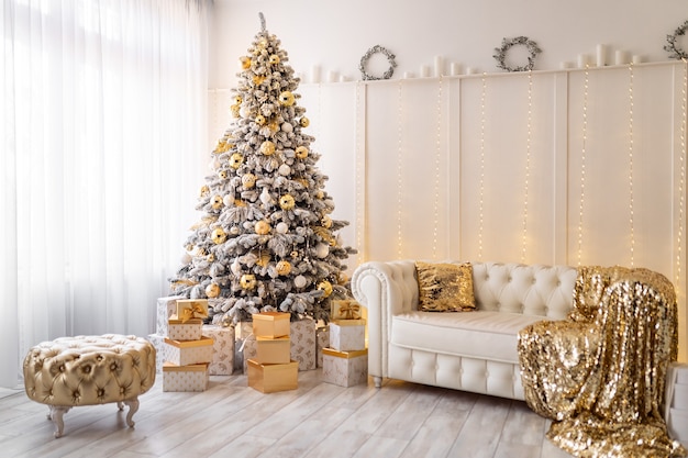 Interior de Navidad blanca con árbol de año nuevo decorado con regalos textiles de puf dorado debajo del árbol