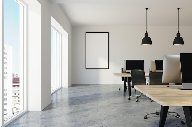 Interior de oficina blanco y contemporáneo con suelo de hormigón y filas de ordenadores con pantallas en blanco sobre escritorios de madera. Un póster simulado con marco en la pared. representación 3d