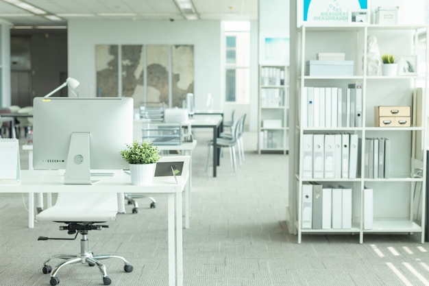 Interior de una oficina moderna con computadora y muebles blancos.