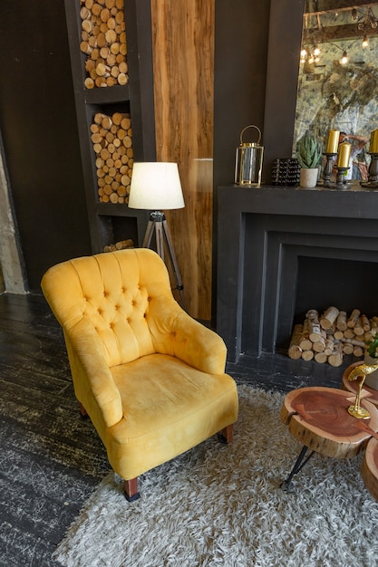 Interior oscuro y brutal de la sala de estar decorada con troncos de madera. sillones suaves amarillos y grises, ventana de arco enorme y chimenea